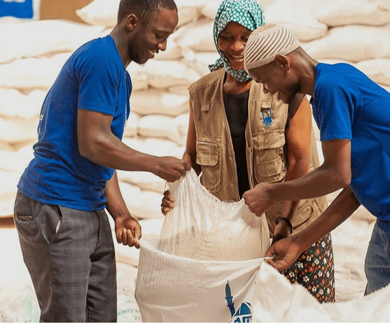 Image of 3 people smiling while helping each other handle a sack of rice